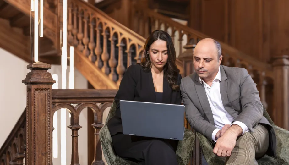 Un homme et une femme consultant un ordinateur portable, assis dans un escalier en bois, pour constituer un patrimoine