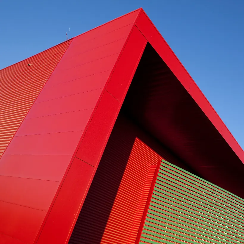 Détail architectural de la toiture rouge triangulaire et de la façade ajourée verte d'un bâtiment