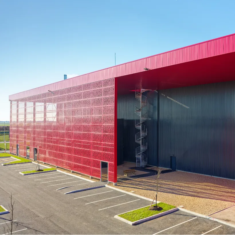Bâtiment industriel à façade rouge ajourée, avec escalier en colimaçon extérieur